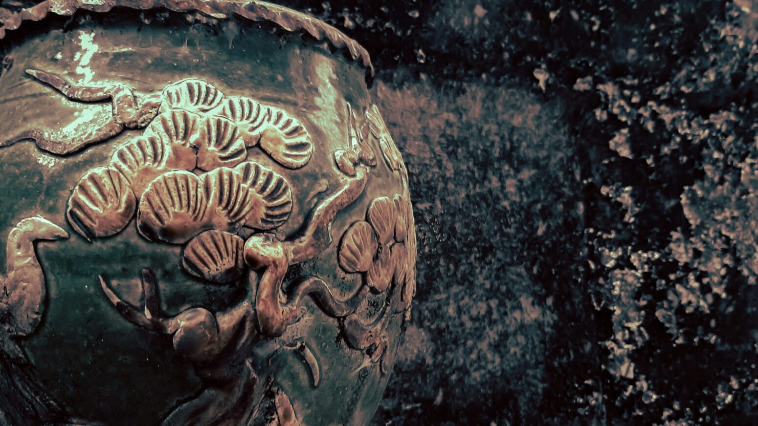 A closeup of a tarnished but shiny vase with sea scenes engraved on it