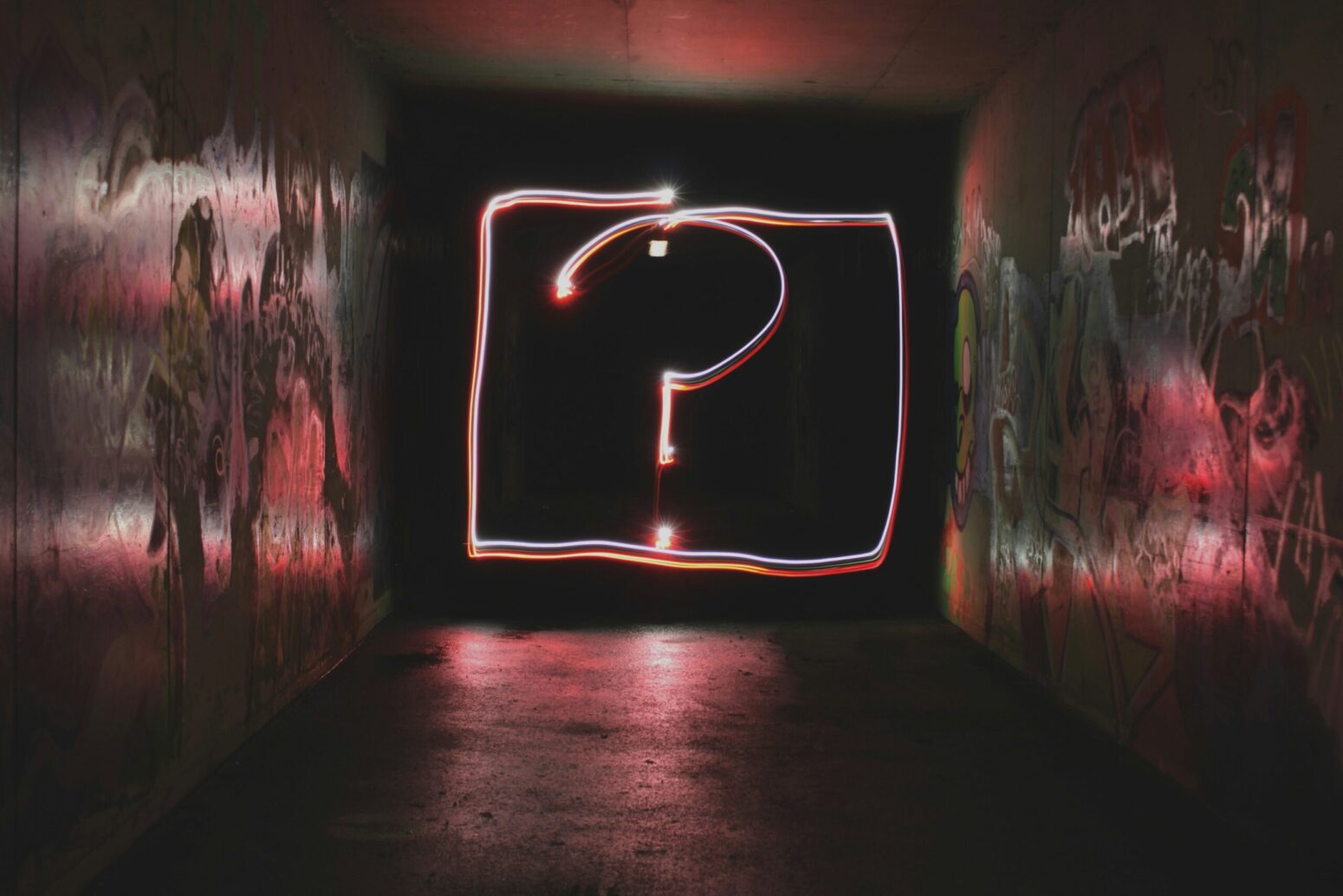 This photograph captures graffitied walls with a neon signage question mark, being lit in the middle.