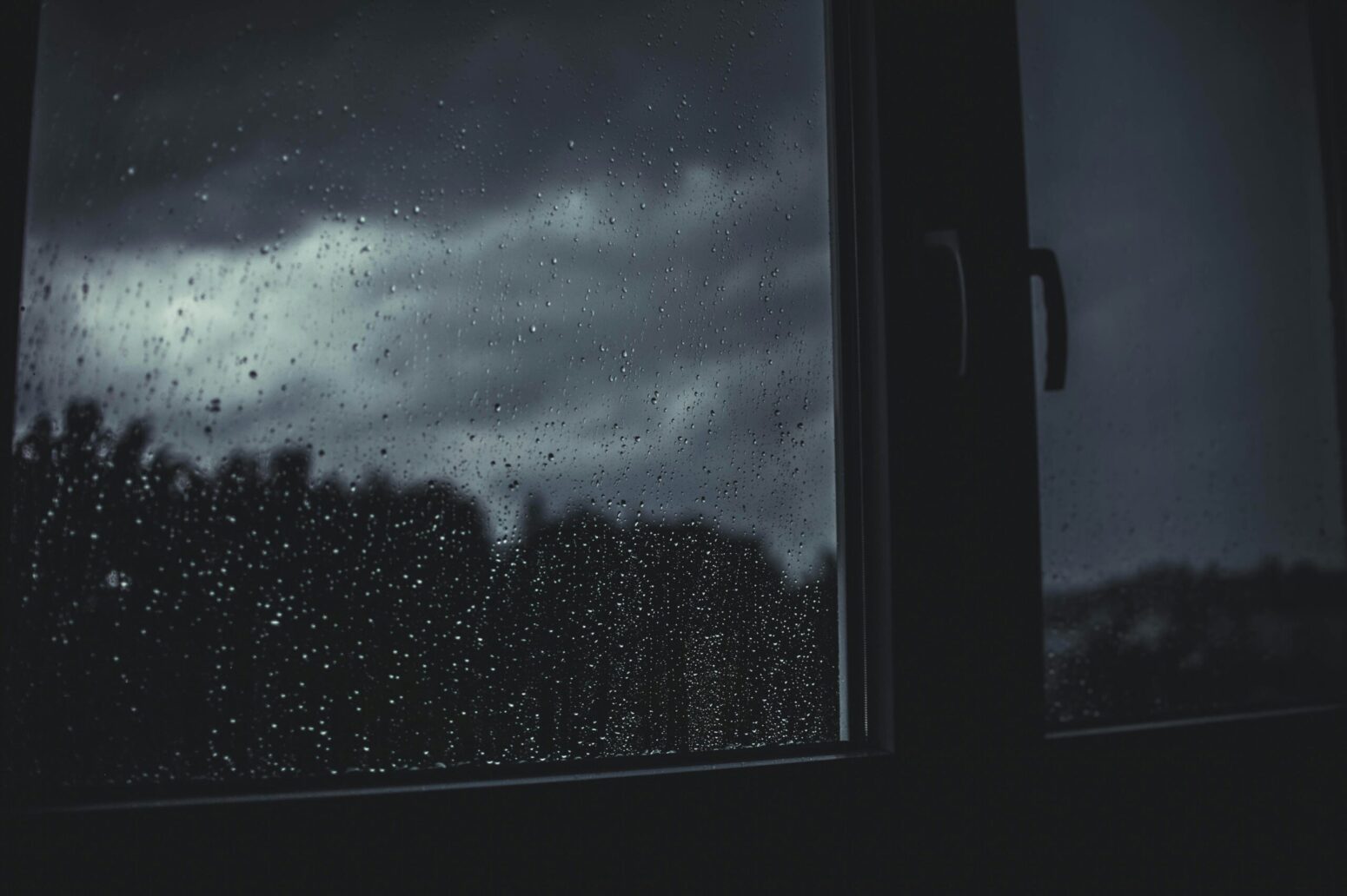 This photograph shows a window with rain drops on it, showing incoming bad weather. Presumably, a thunderstorm, or something worse.