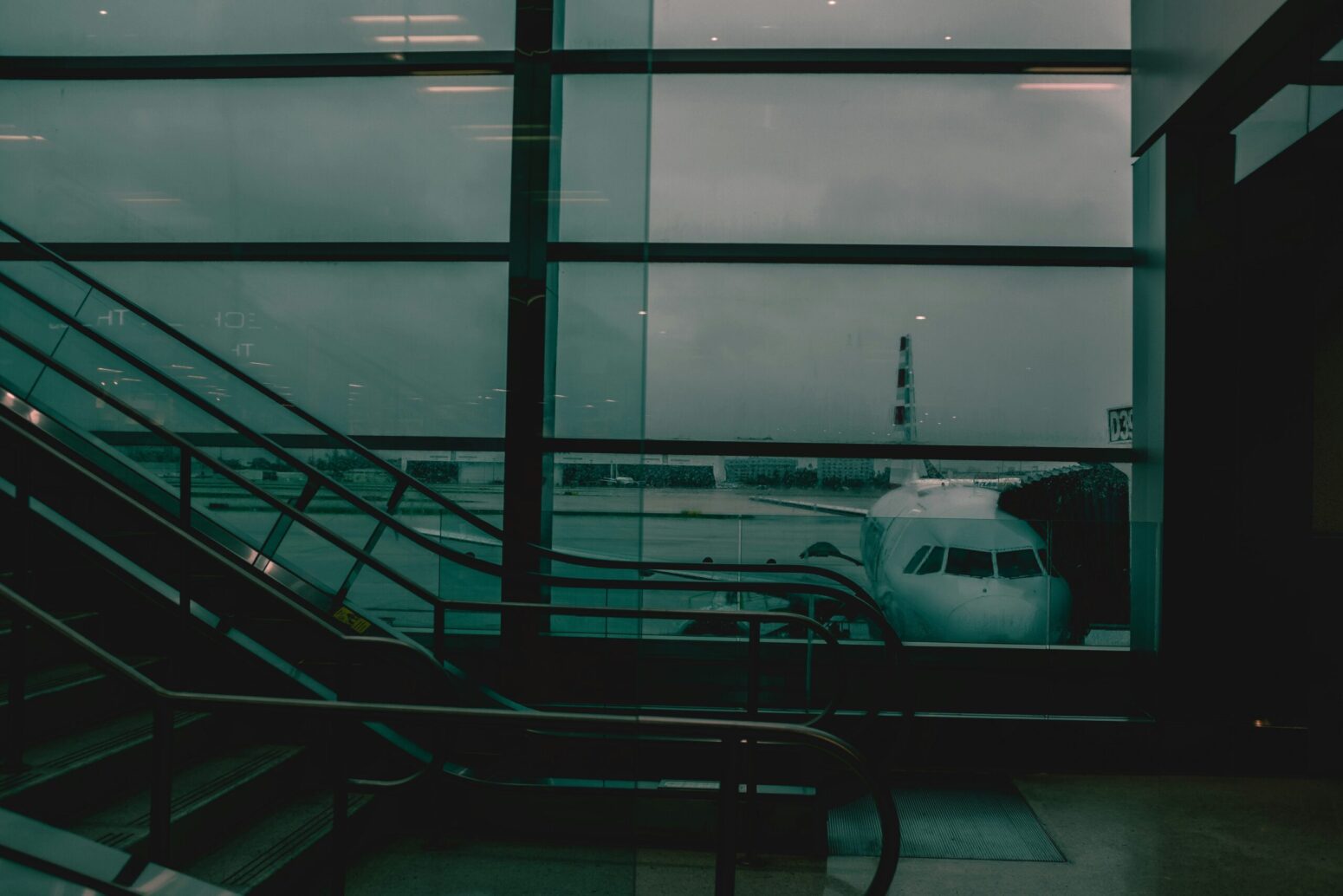 This photograph shows an airplane through several glass panes at an airport. The photograph is a mixture of blue and gray.
