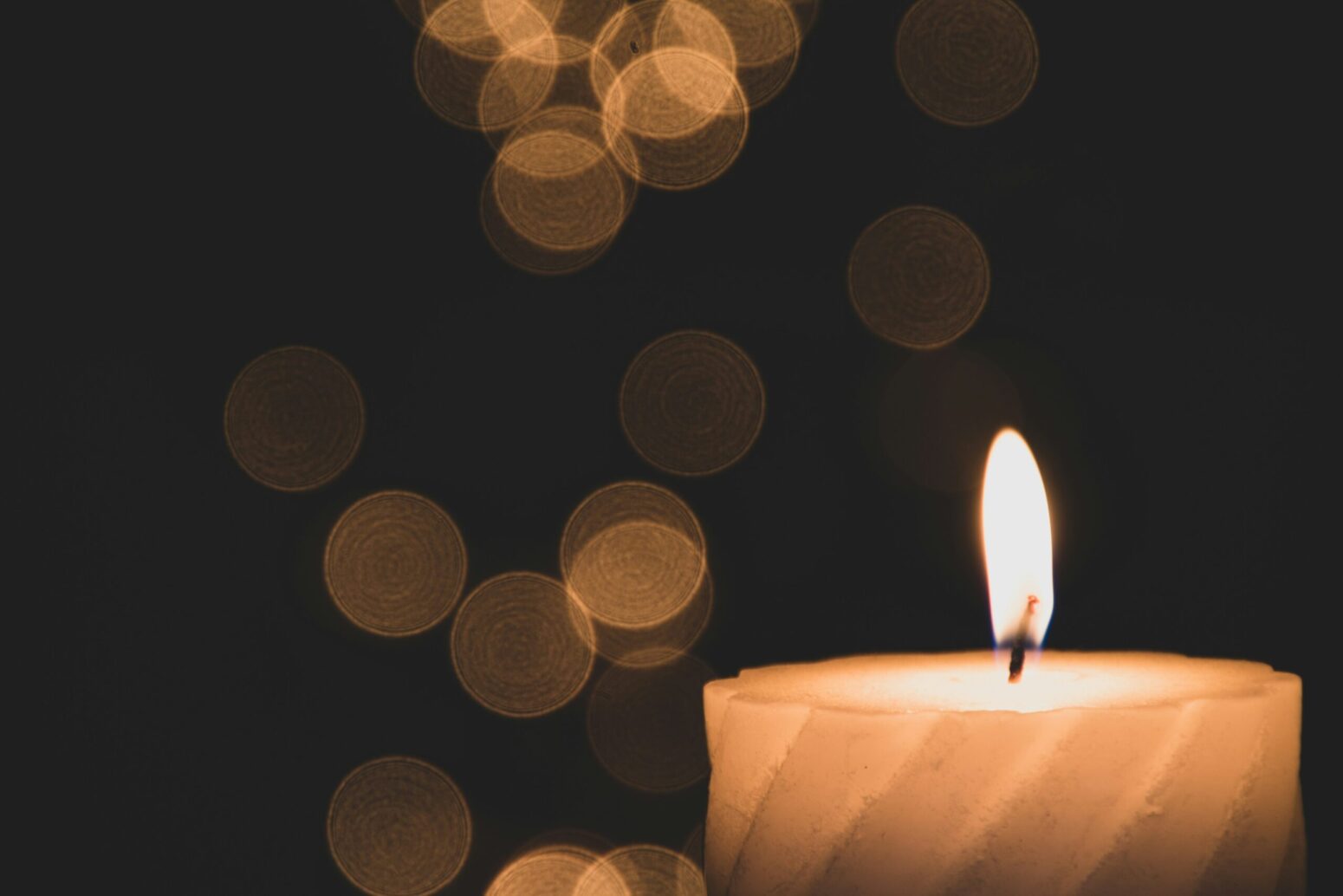 This photograph shows a faint orange glimmer of light in the background, with a lit candle being the focus.
