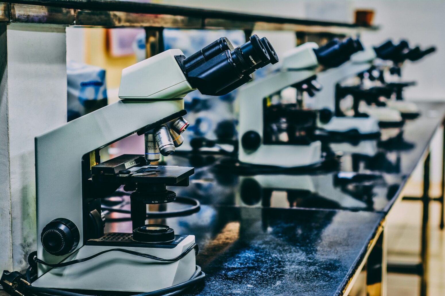 This photograph shows several white microscopes on top of a black counter. This photograph was presumably taken in a science class.