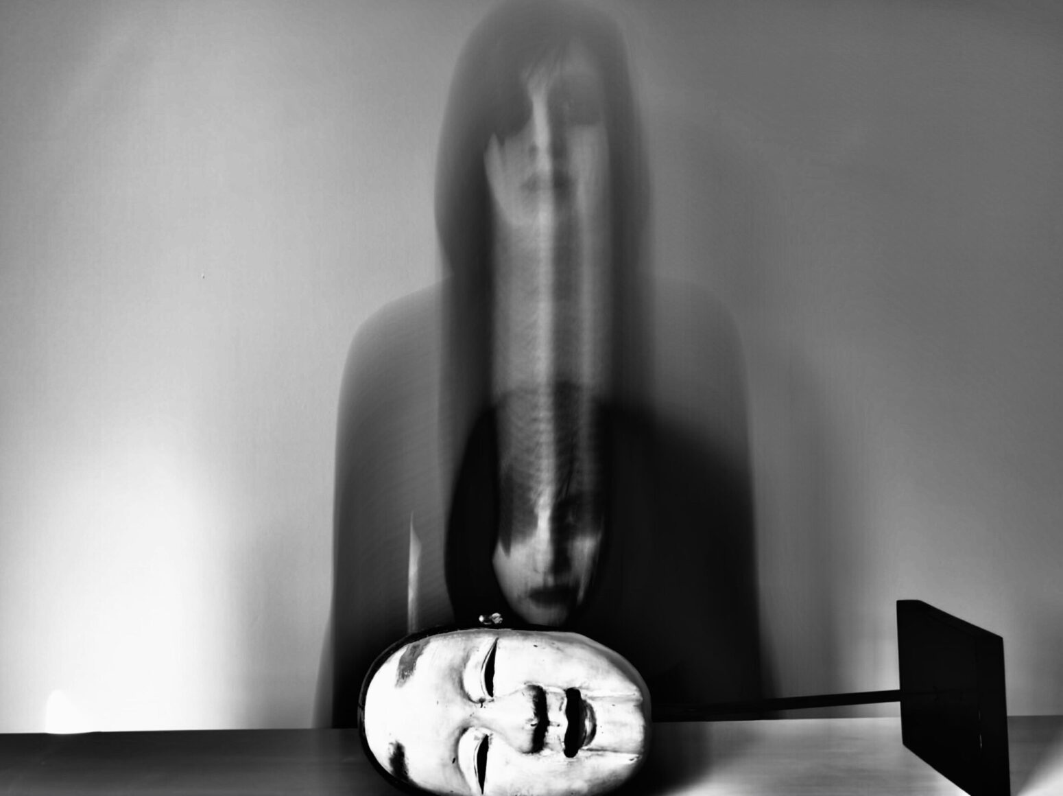 This photograph shows a black and white man with a hat figurine. The photograph is intentionally blurred, with the man wearing makeup.
