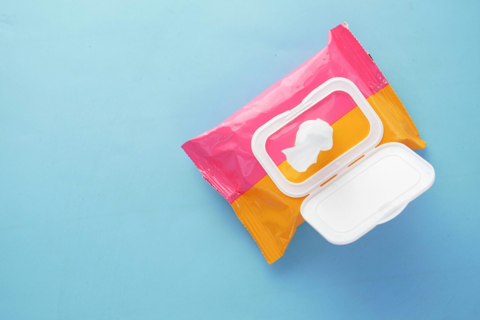 This photograph shows a pink and yellow pack of wipes that rests neatly on a light blue surface.
