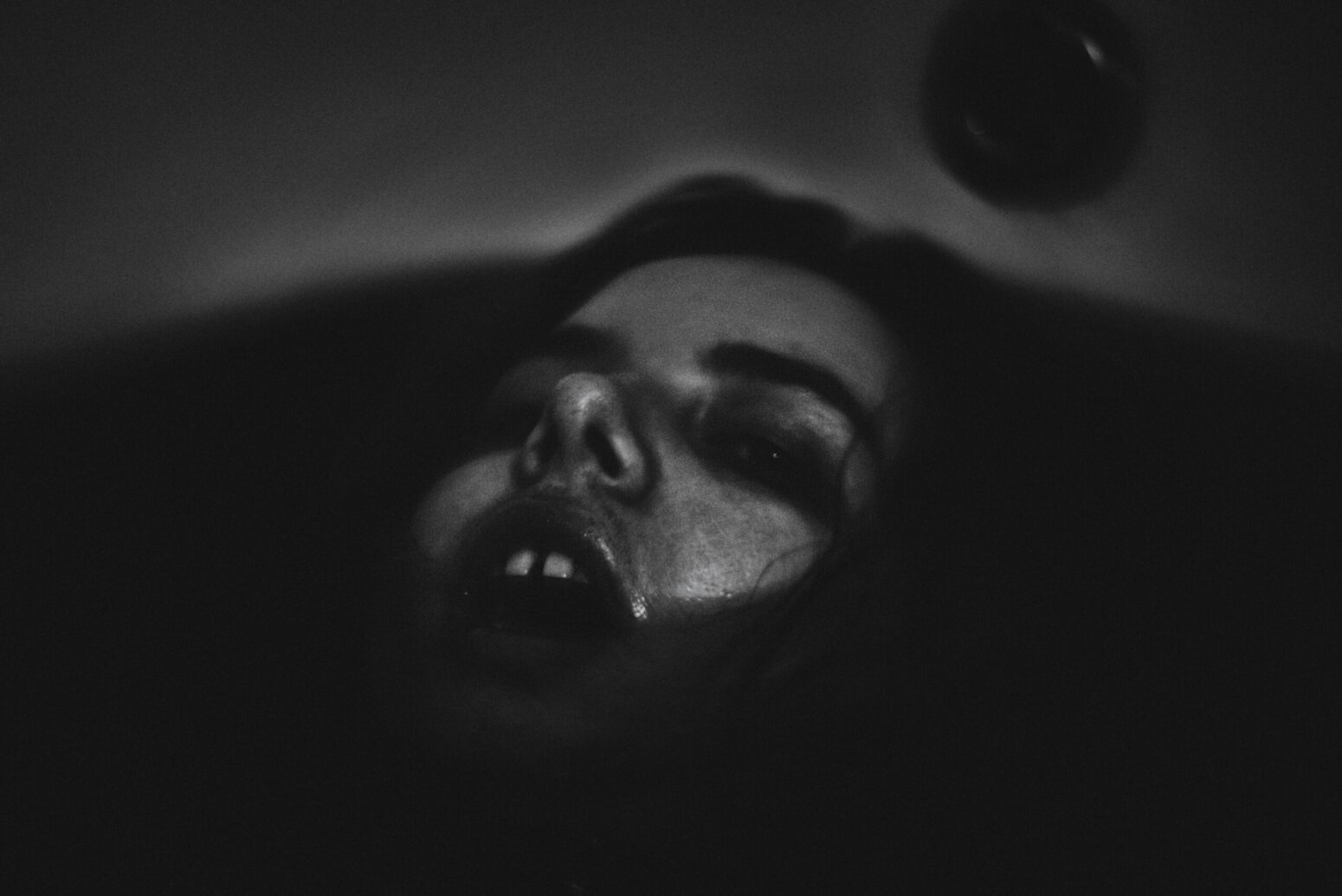 This photograph shows a person's face being submerged in dark water.