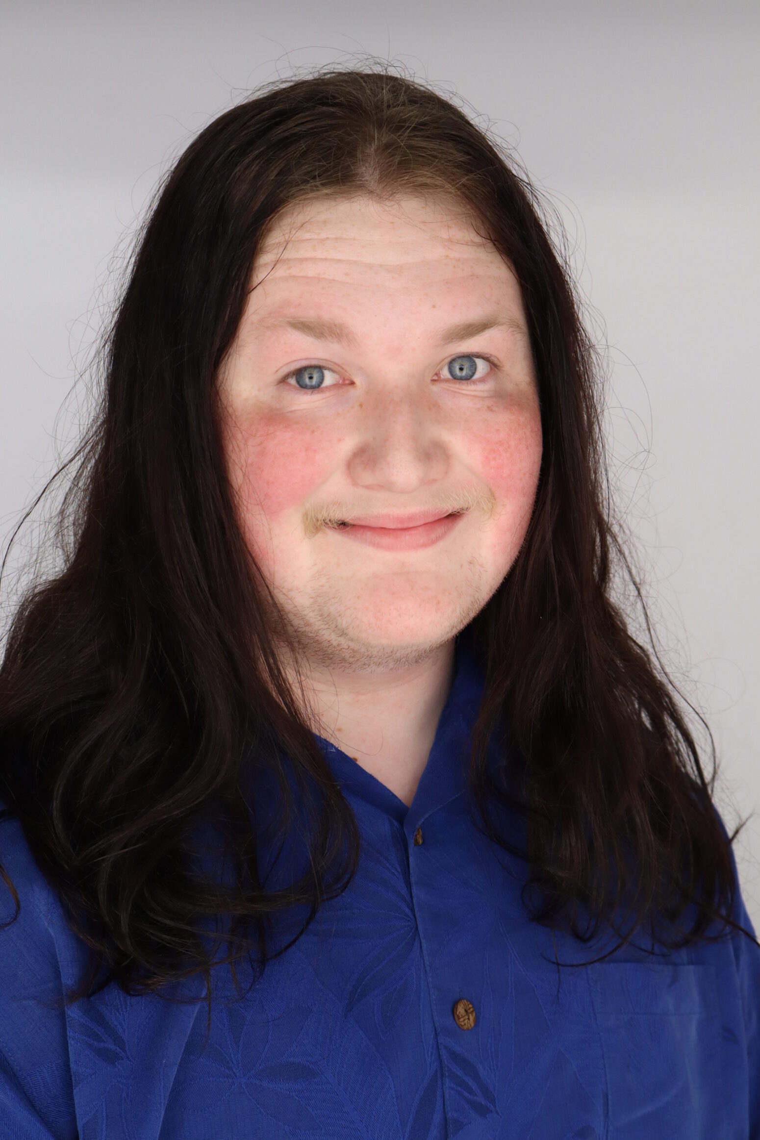 Anthony Brown, a white man with long, dark hair, wears a blue shirt and smiles.
