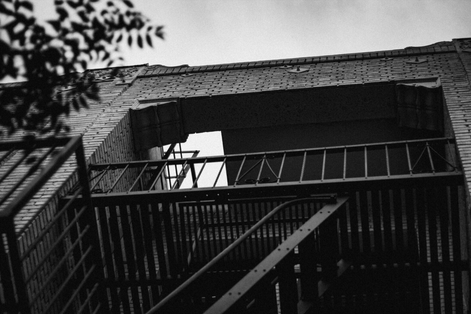 This black and white photograph shows some sort of apartment complex, with the cloudy sky illuminating the awning and fencing.