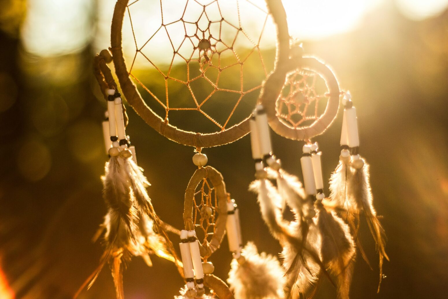 This photograph shows a dreamcatcher hanging in the air with a splash of golden yellow from the sunset in the background.