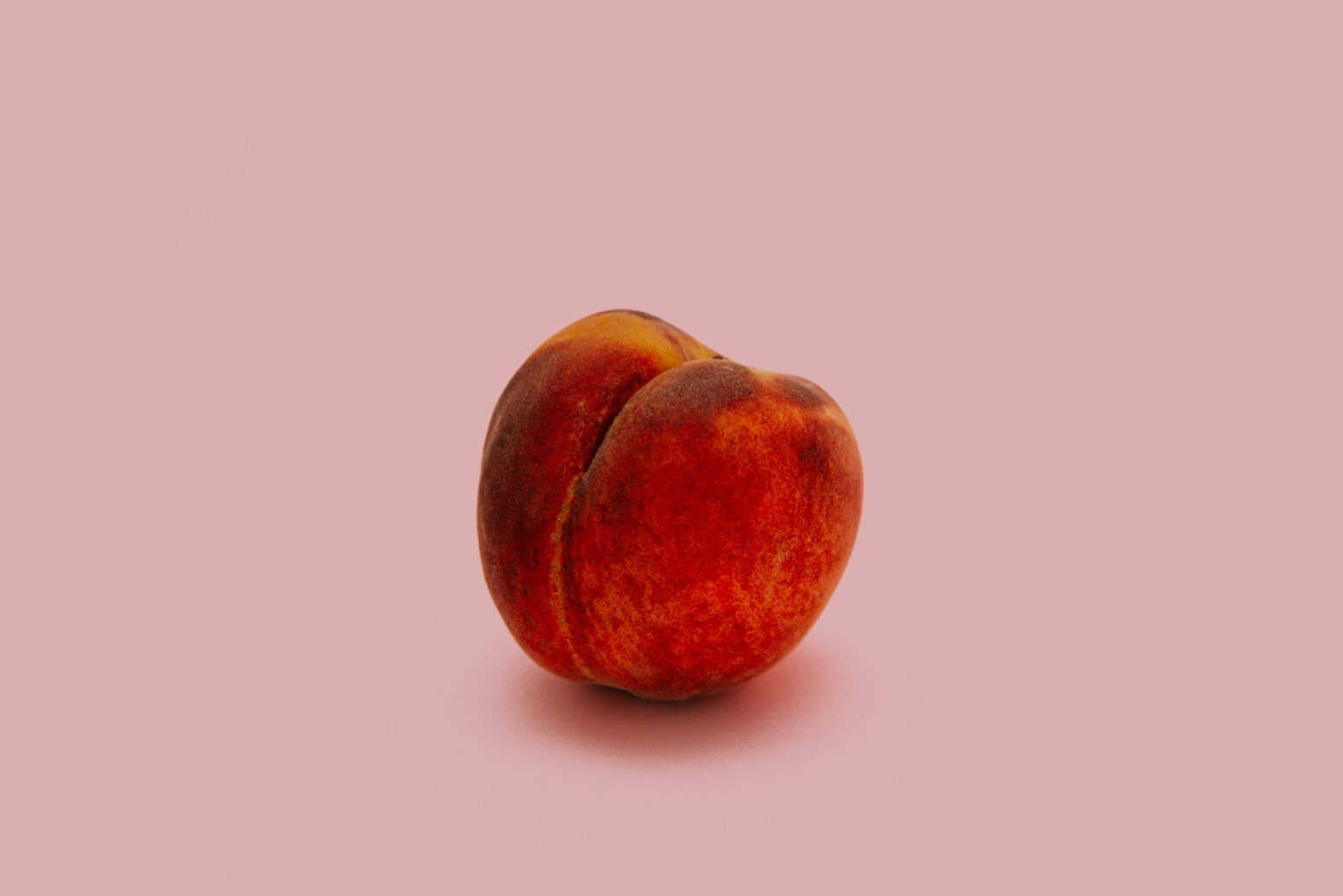 This photograph shows a peach in a light pink background.
