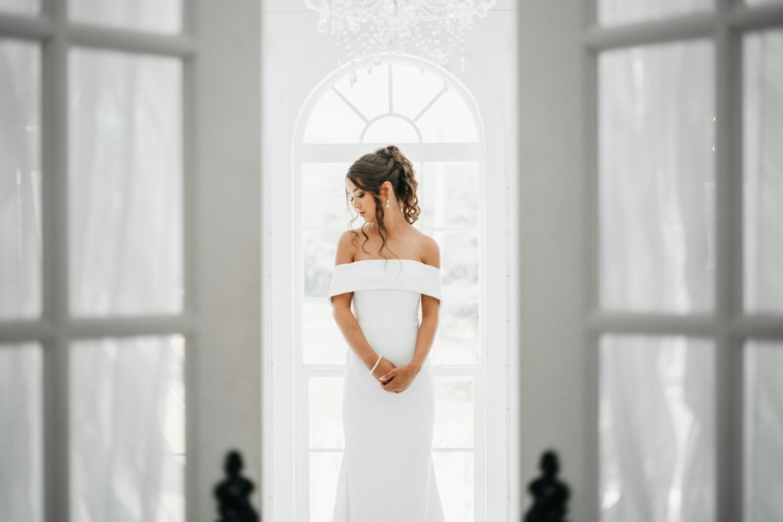This photograph shows the inside of a white building with a woman in a white dress, looking down to her right.