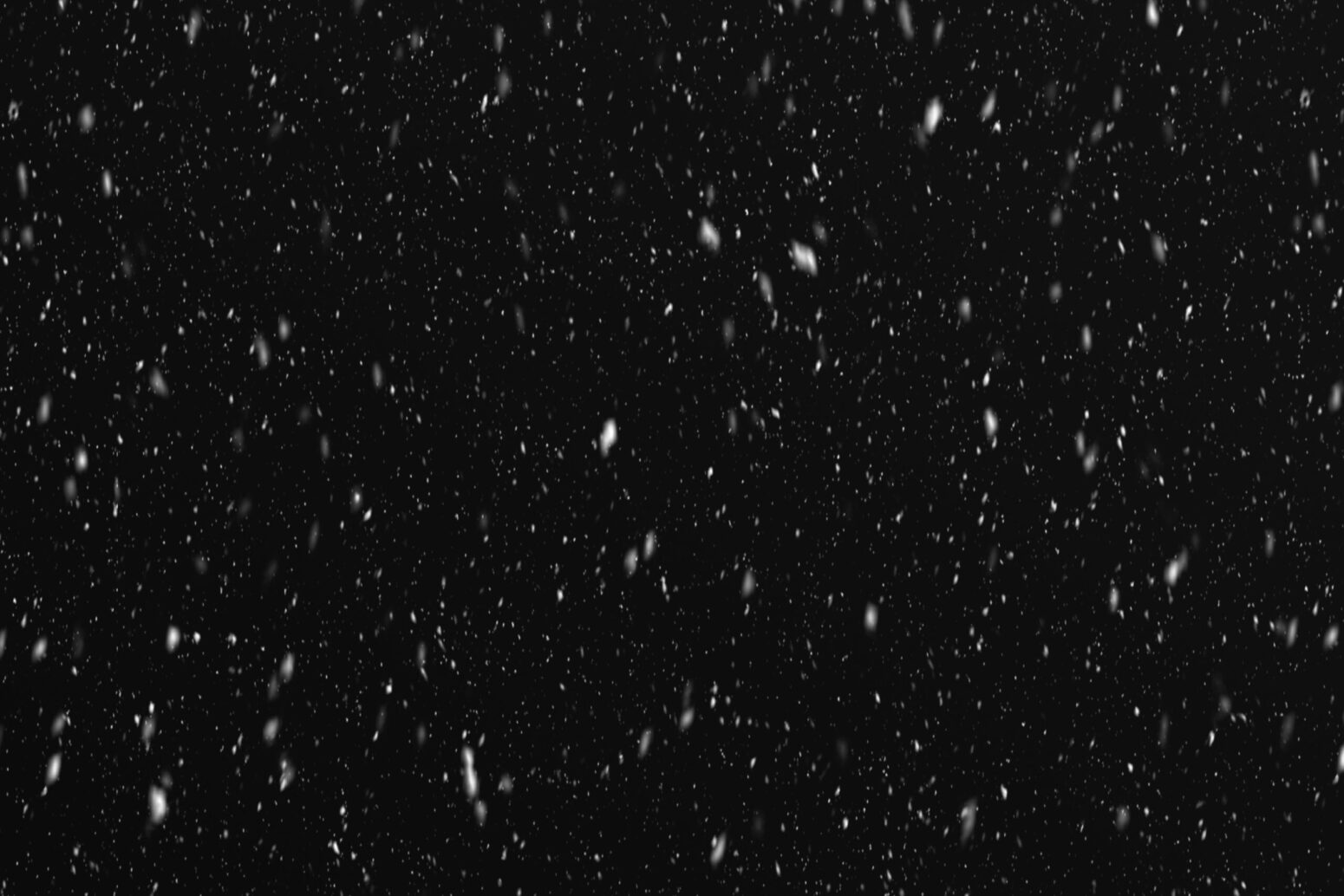 This photograph shows a dark sky with snow falling to the ground.
