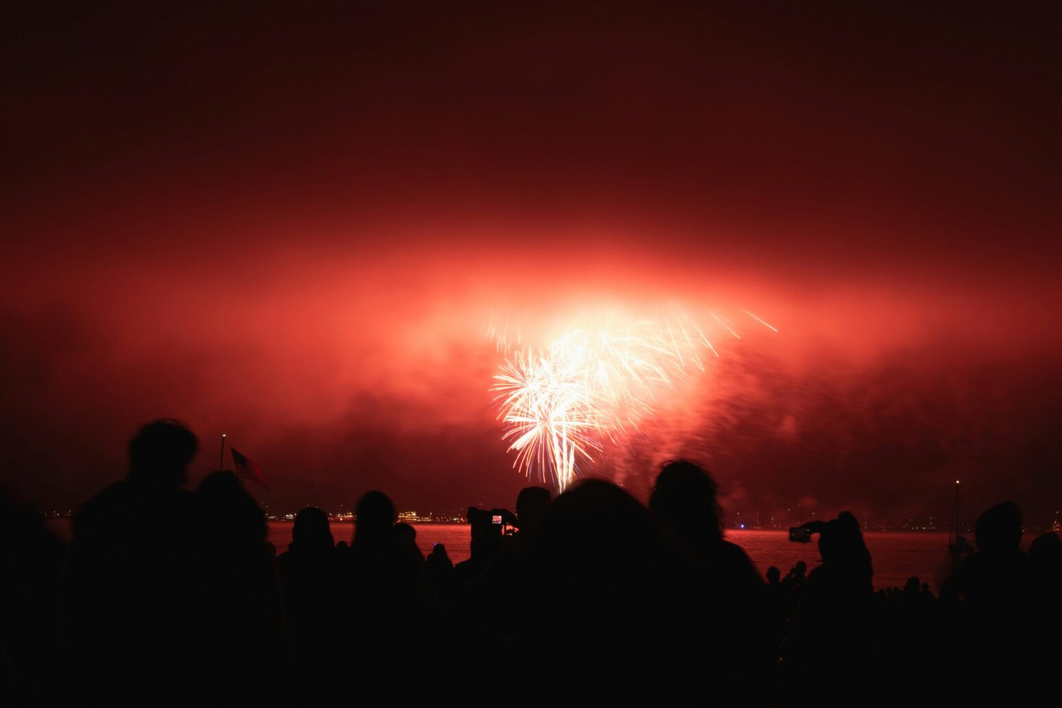 This photograph shows a red firework, with the shadows of many people being present within the photograph.