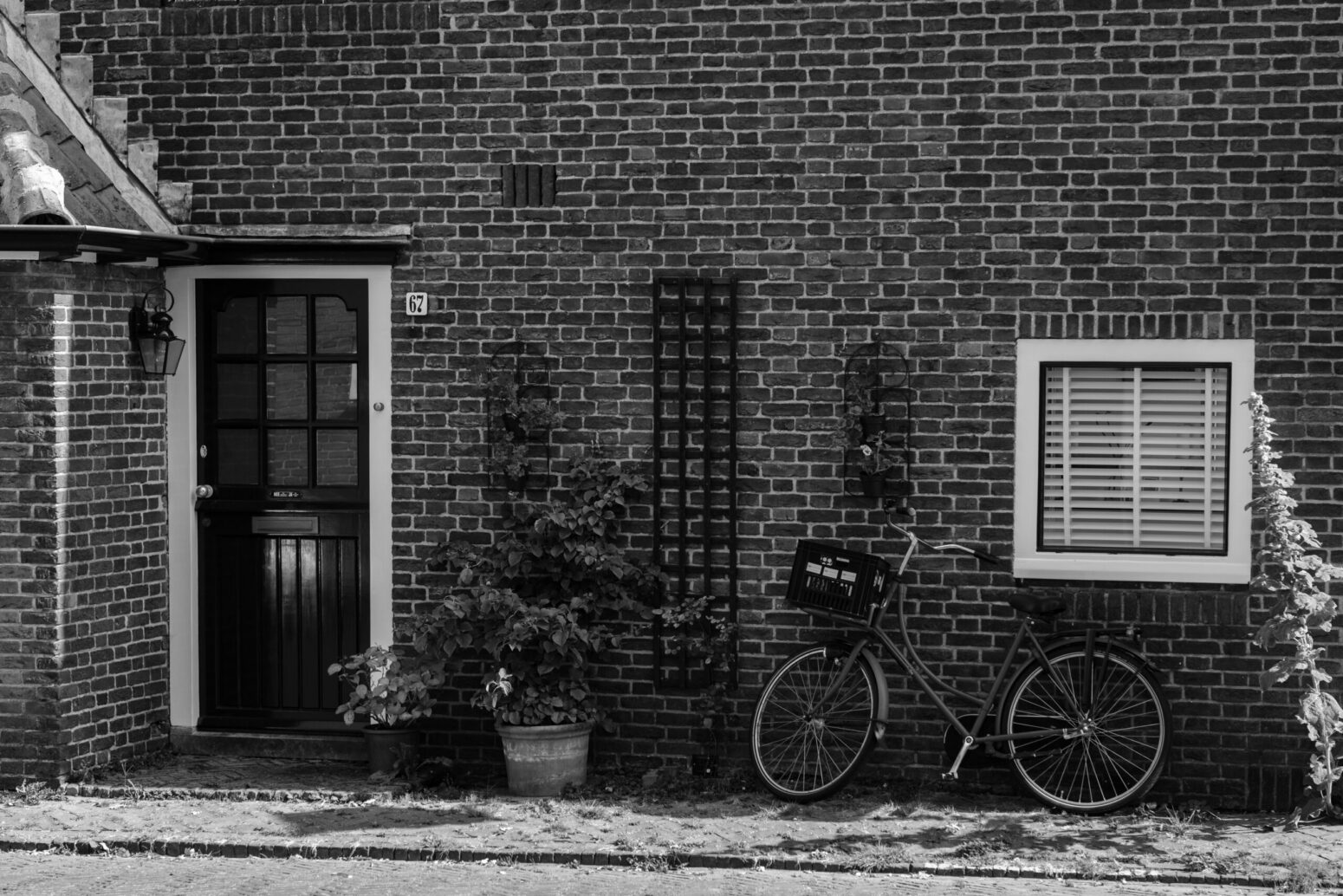 This black and white photograph shows a brick house with a door, window, bike, and other things that are seen in the photograph.