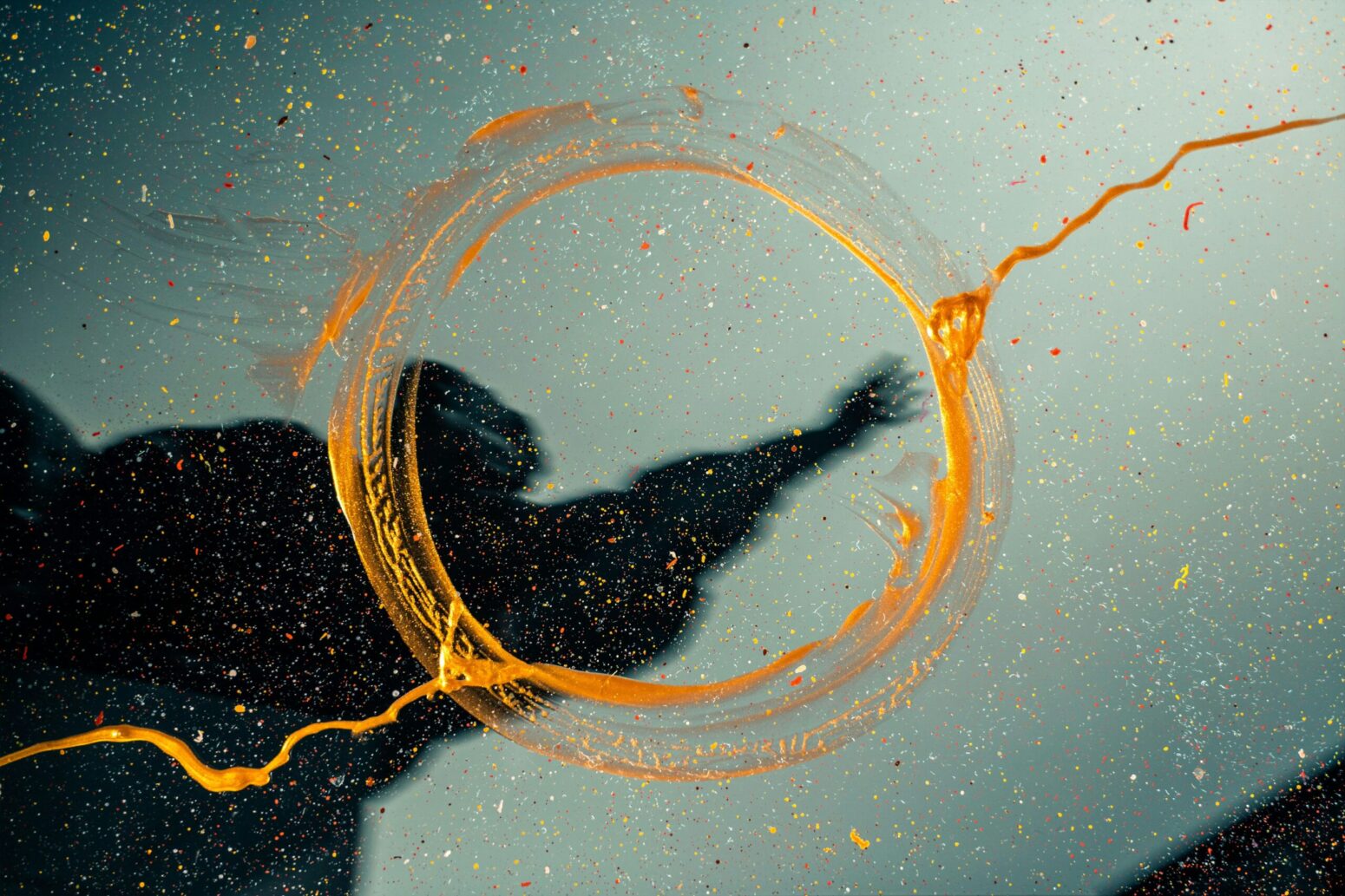 This photograph shows a sort of gold painted circle in the water, with a hand reaching through being visible in the middle of the circle.