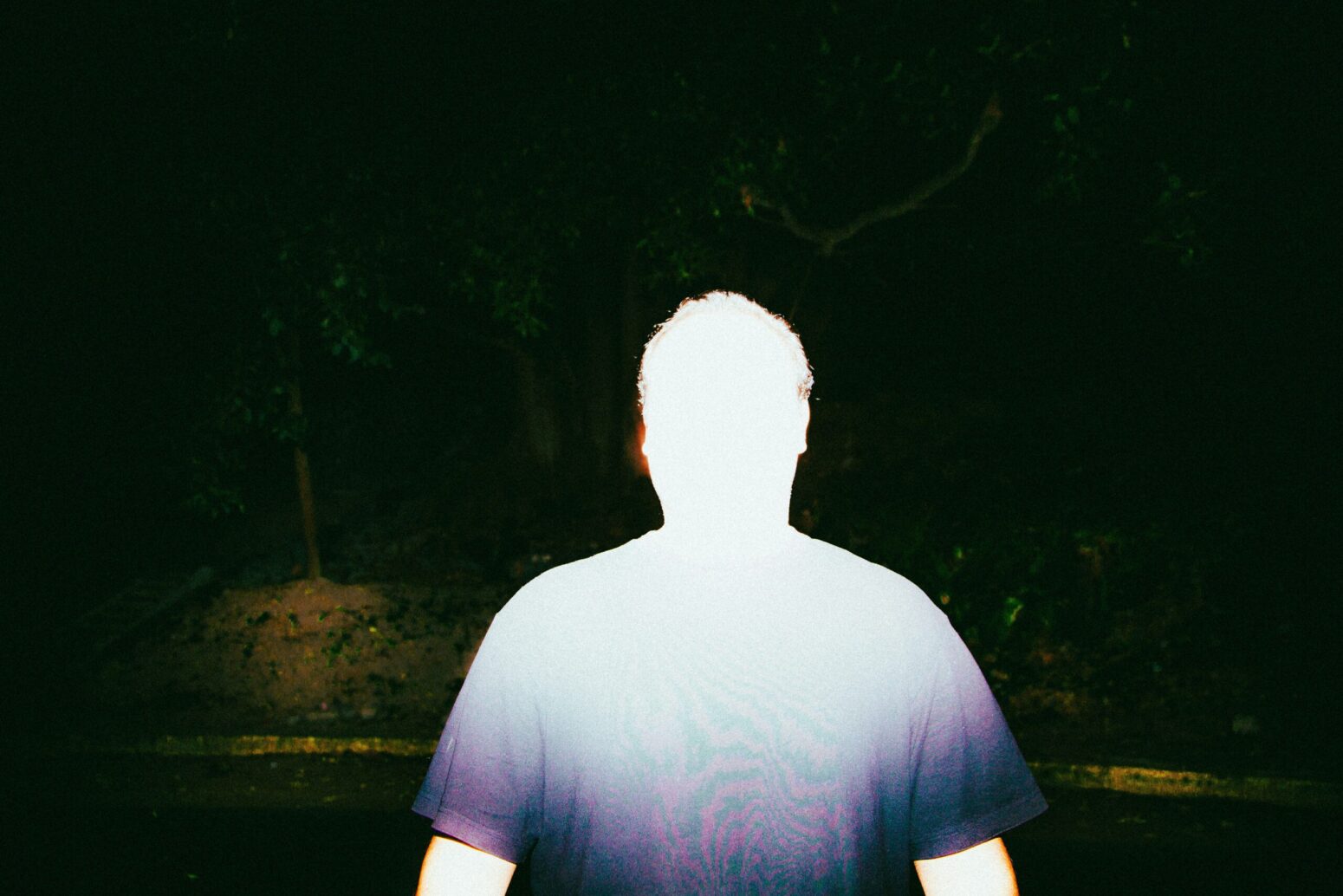 This photograph shows a person who is blinded by the light, with a dark forest, of sorts, being present in the background.