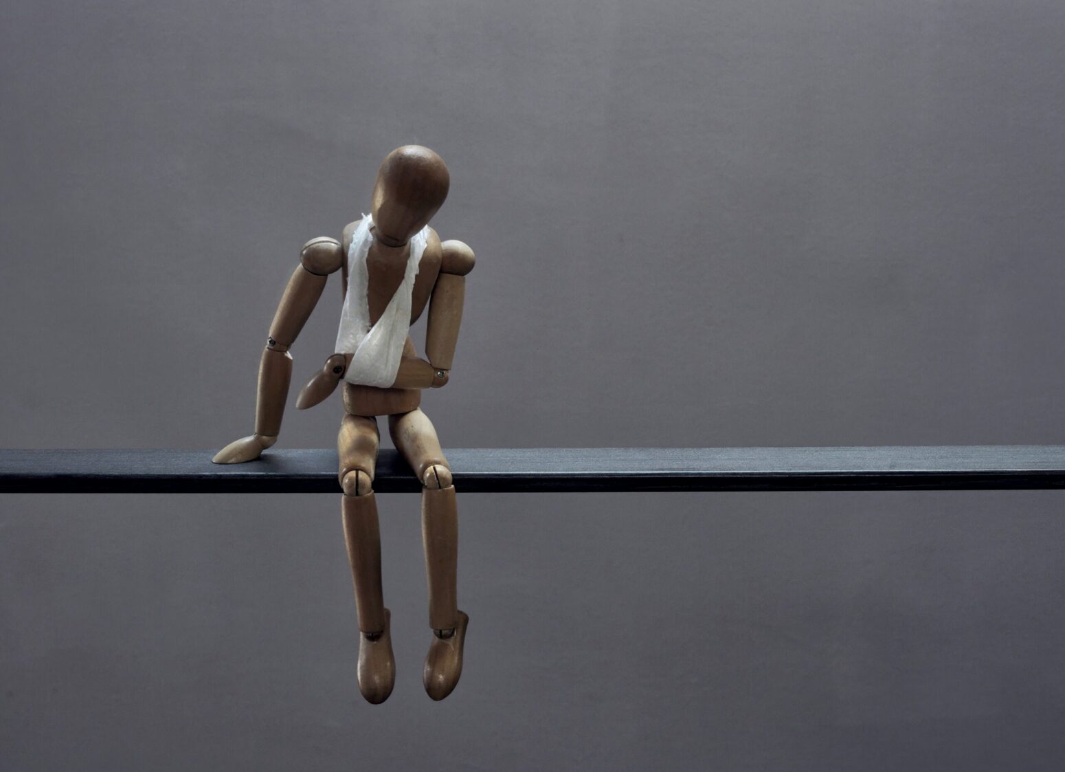 This photograph shows a doll with an arm patch, presumably with it's arm broken, sitting on a ledge with a gray background.