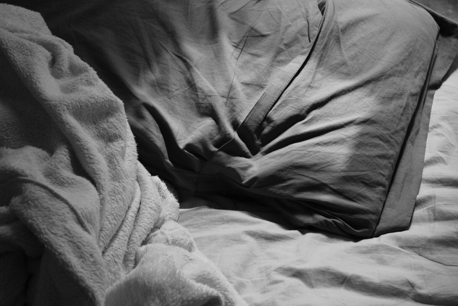 This photograph shows gray bedsheets and a gray pillow, with the bed being unoccupied.