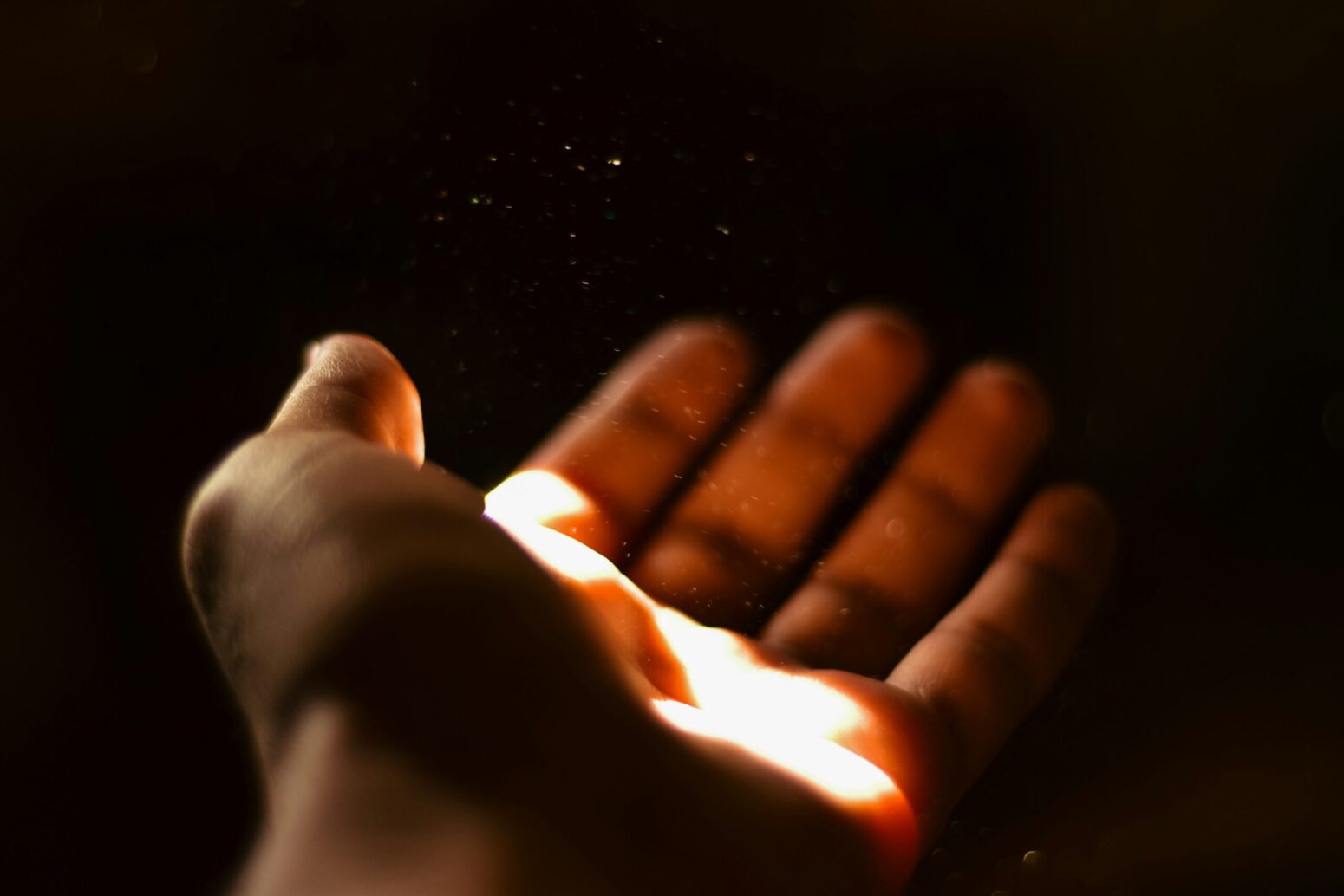 This photograph shows a hand with a glimmer of darkness, with what seems like a sort of gold powder right above the hand.