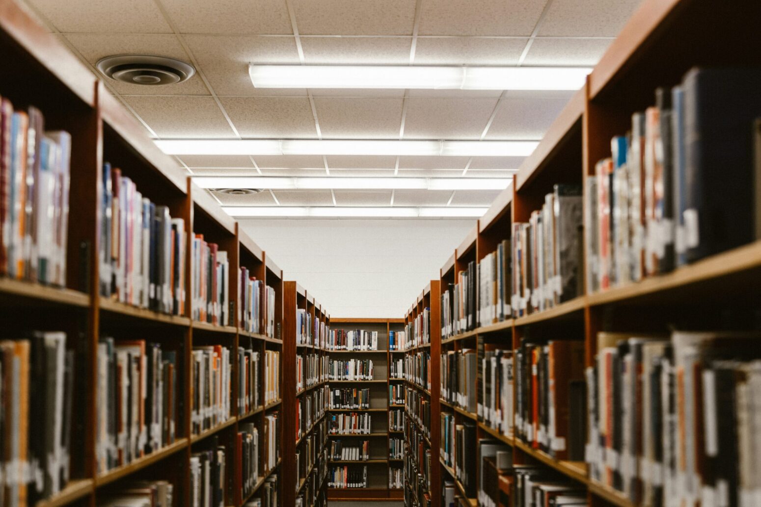This photograph shows a school library with bookshelves filled with books, and lights shining above.