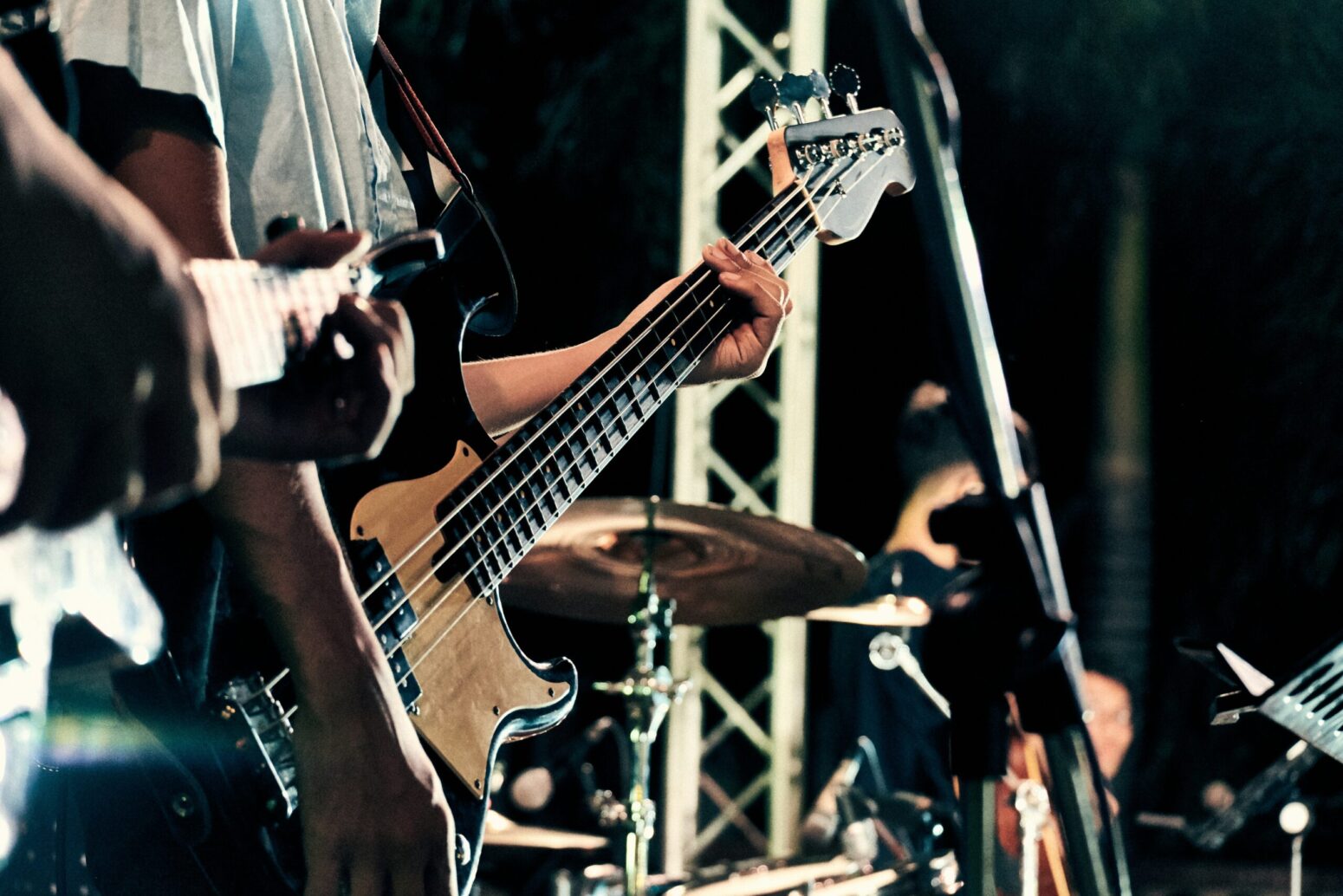This photograph shows a person holding a guitar on a stage with other instruments like drums.