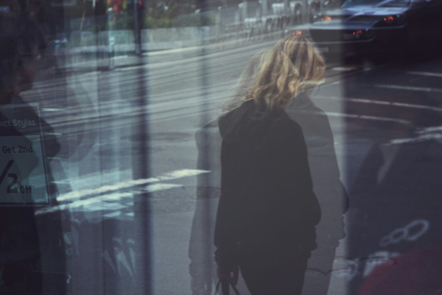 This blurry photograph shows a person walking near the street, with the city being noticeable in the background.