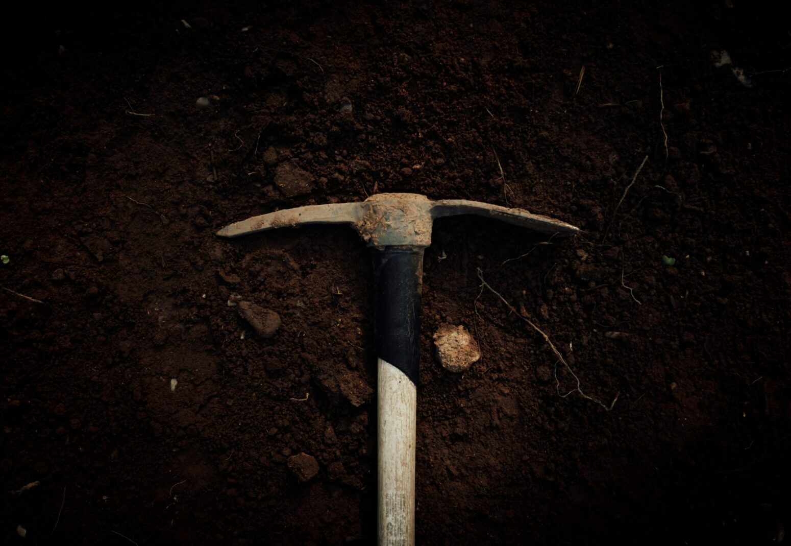 This photograph shows a pickaxe laying on a bed of dirt.
