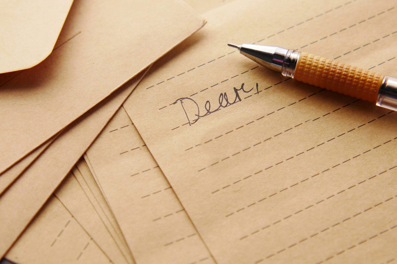This photograph shows several pieces of paper, but with a pen laying on a piece of paper that has "Dear" written on it.