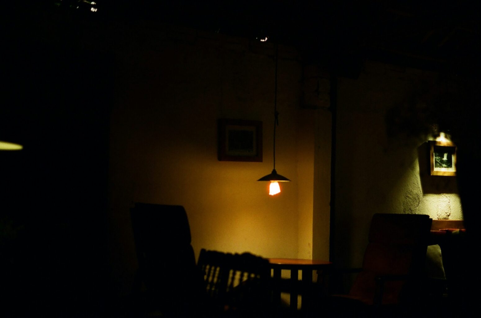 This photograph shows a poorly lit place of what seems to be chairs, tables, within a room of sorts.
