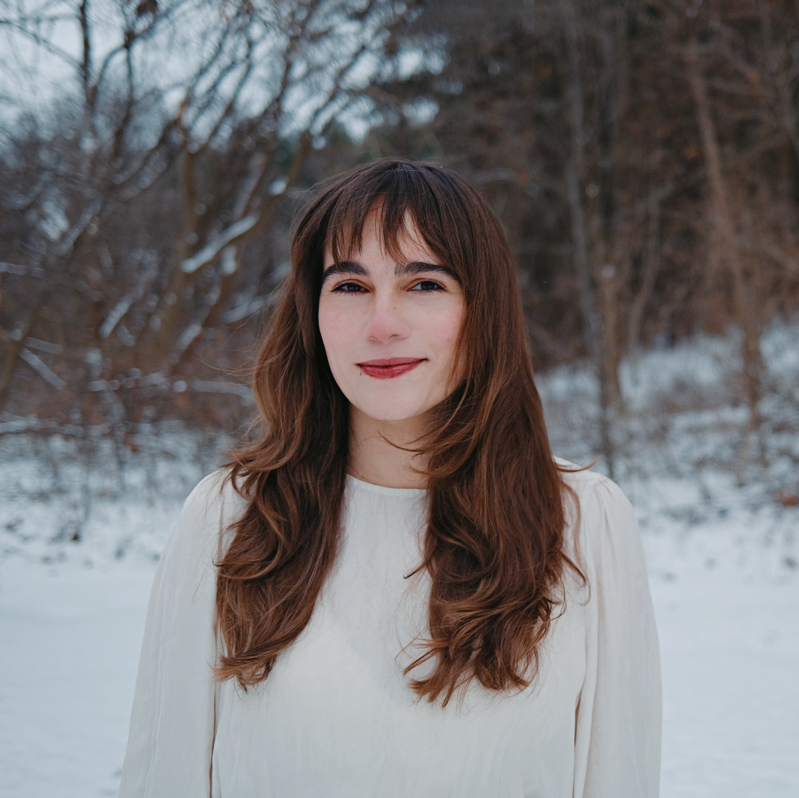 Leila Chatti, a Tunisian-American woman with long brown hair, wears a white sweater in front of a snow-filled landscape and smiles.