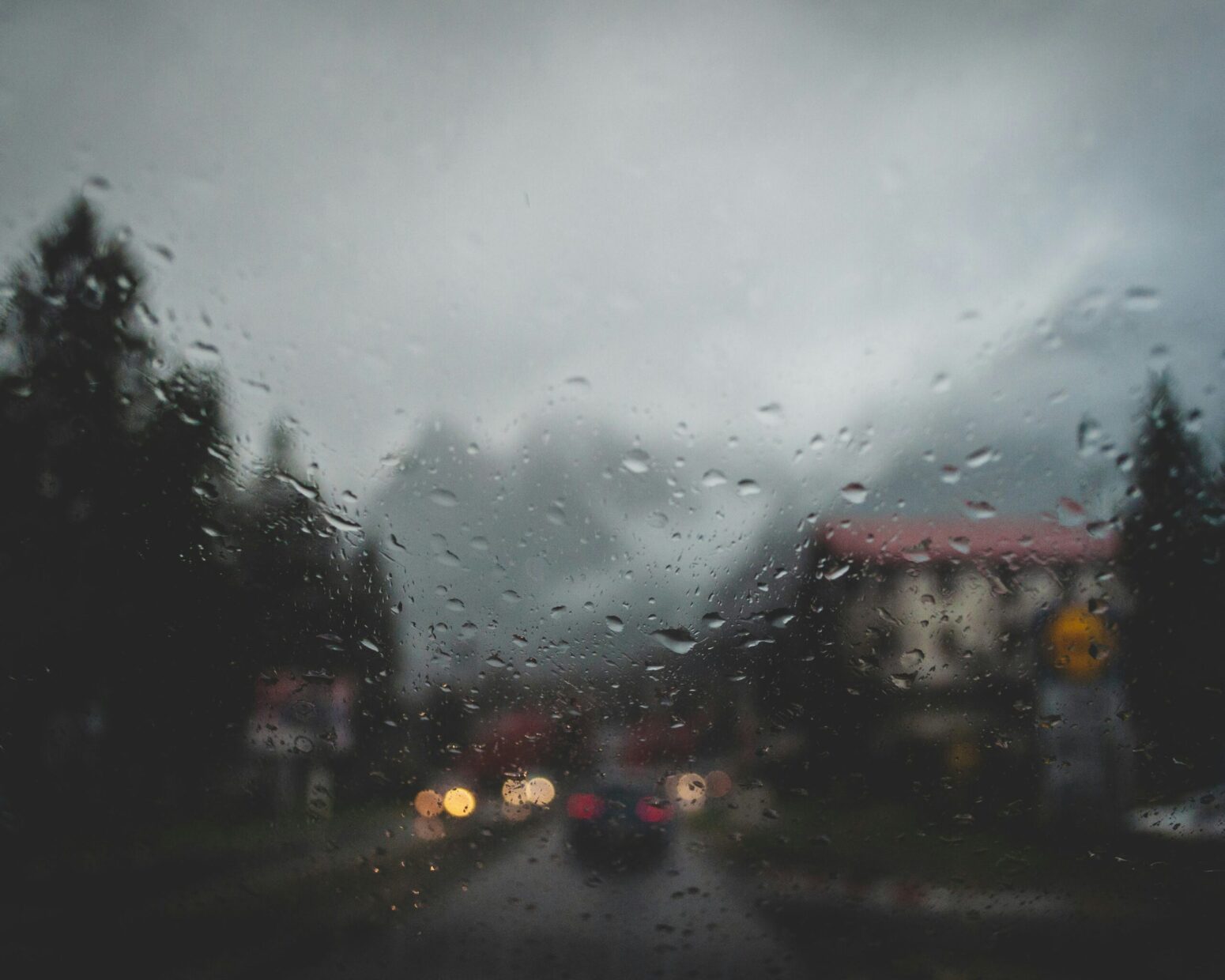 This blurry photograph shows a mountain in the distance, with the car driving in the road with a surrounding town and condensation from rain blurring the image.