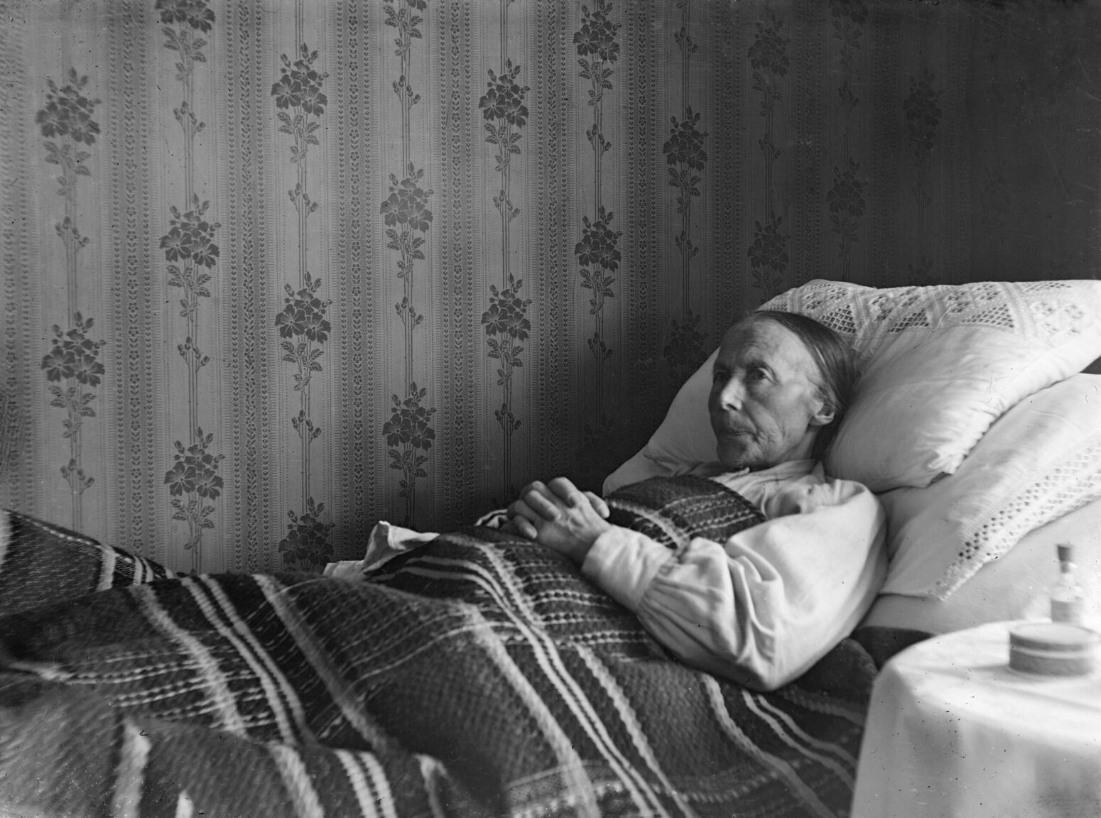 This black and white photograph shows an elderly woman sitting in bed.