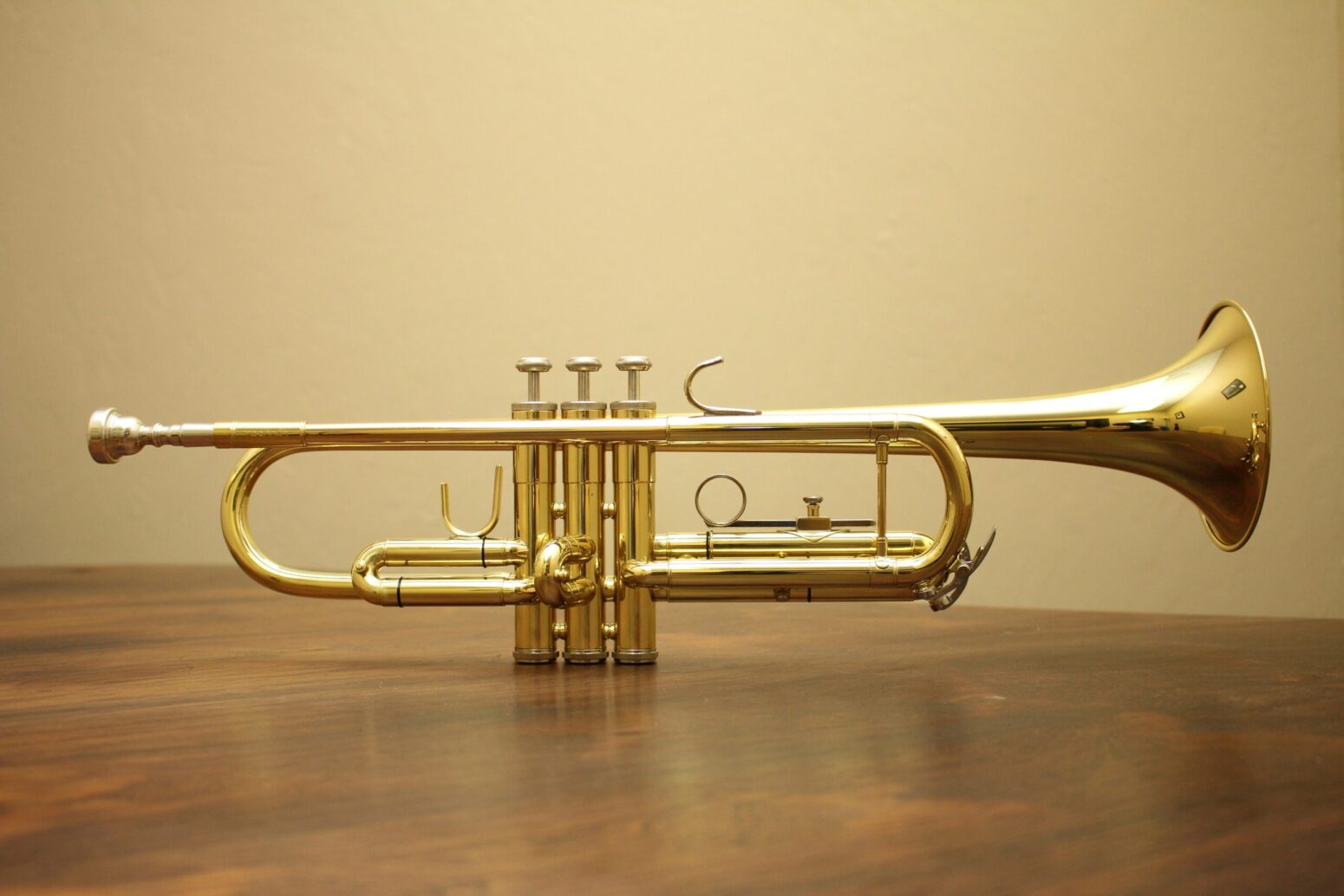 Brass-toned trumpet sitting on a wood surface against a beige background.