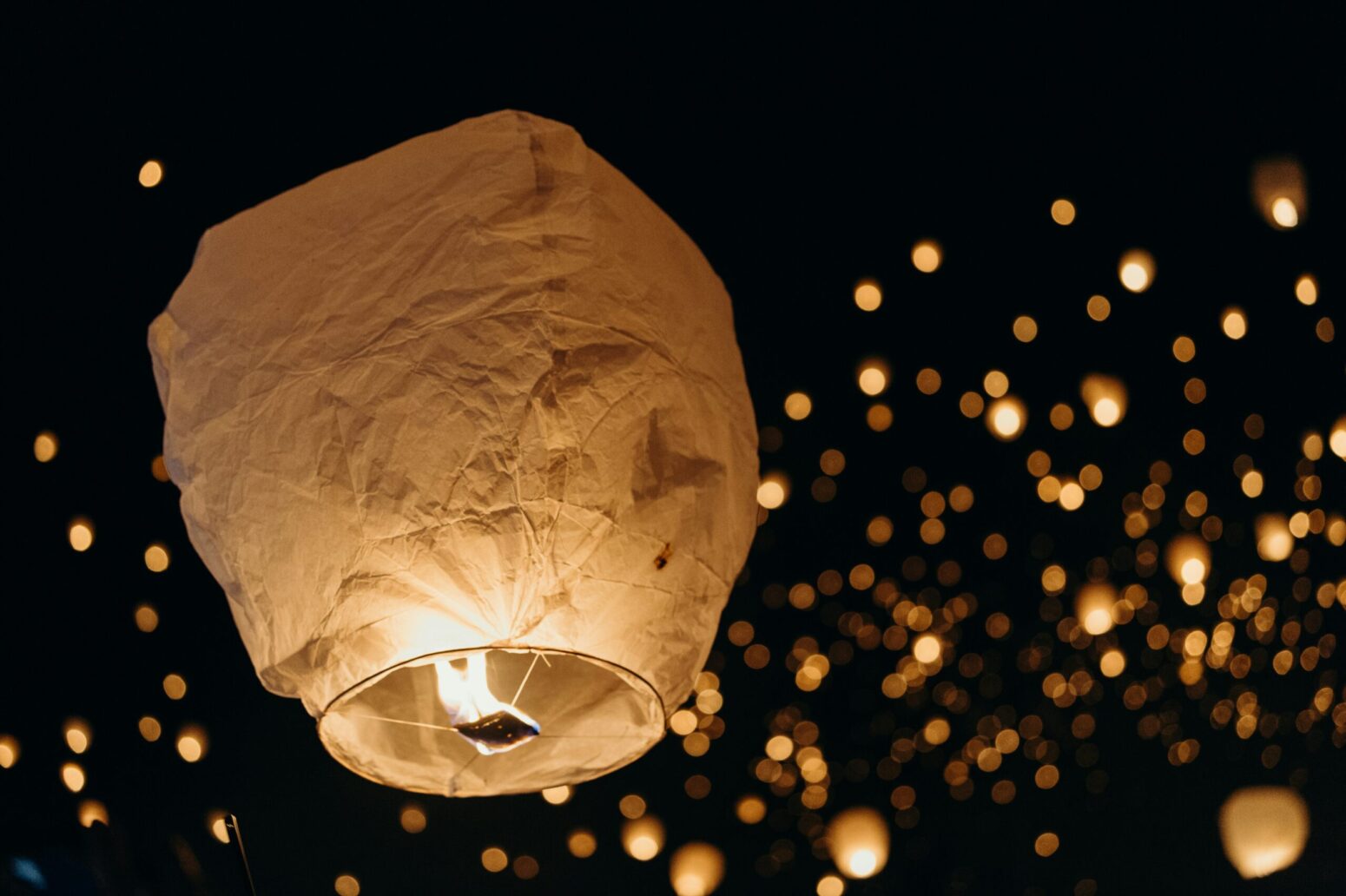 This photograph shows a beige paper lantern being ready to head into the sky, where many other paper lanterns can be seen.