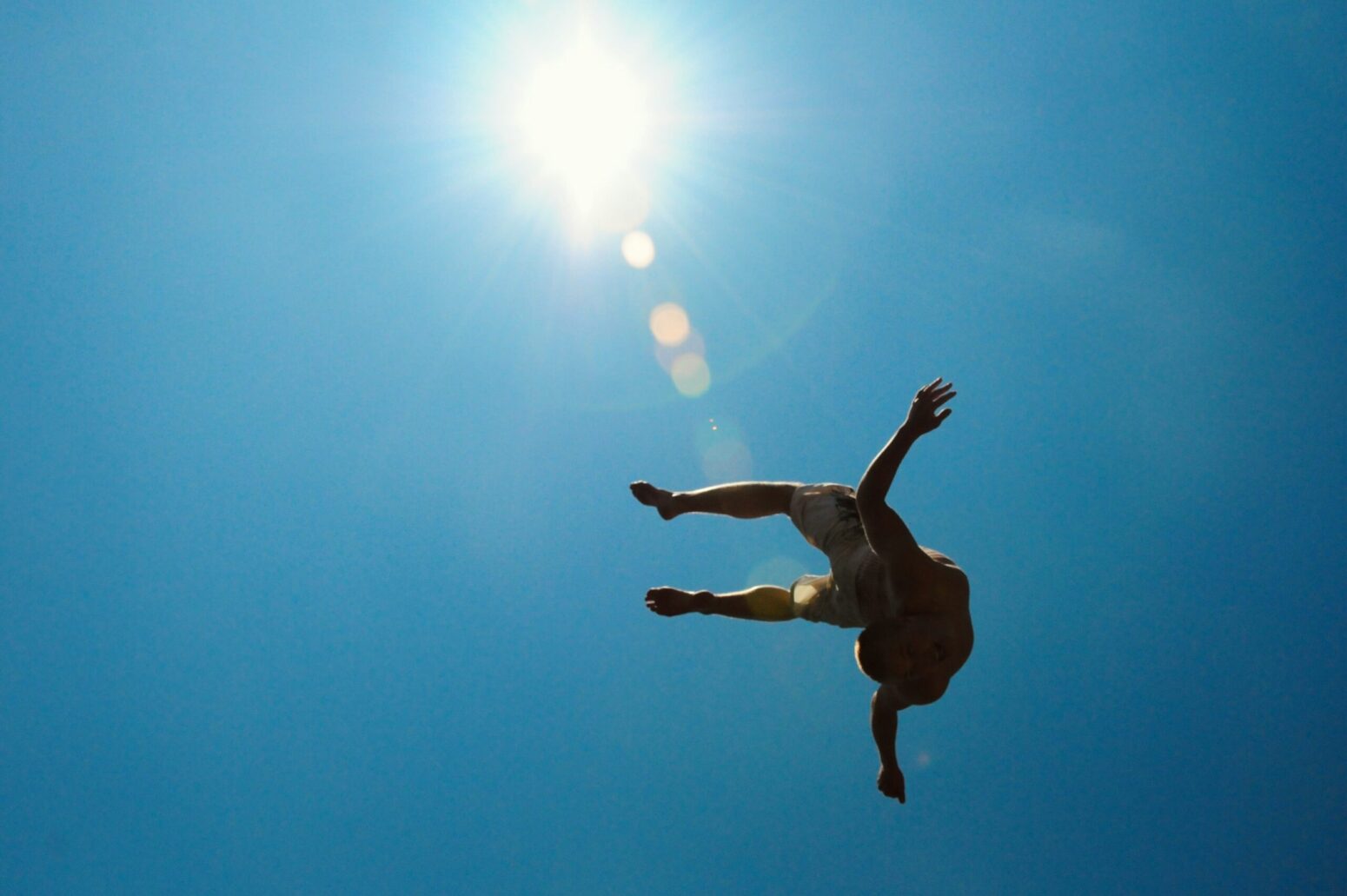 This photograph shows a man falling out of the sky, with the sun gleaming on the surrounding blue sky above.
