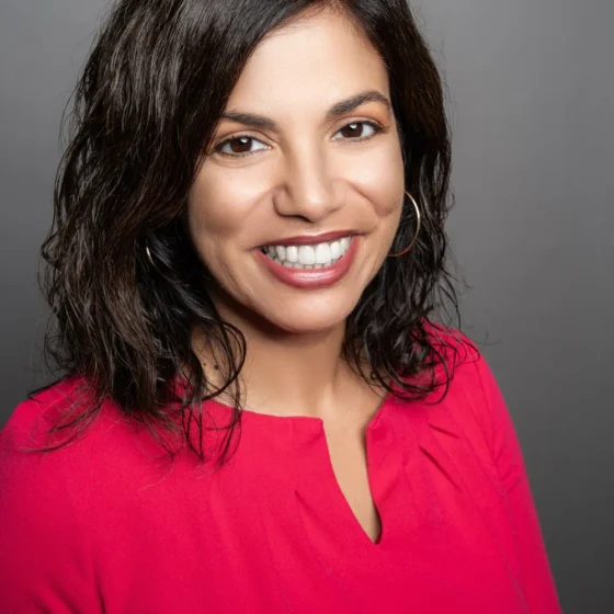 A woman with short black hair wearing a red full sleeved blouse smiling at the camera