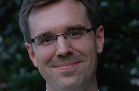 A man with rectanglular glasses smiling