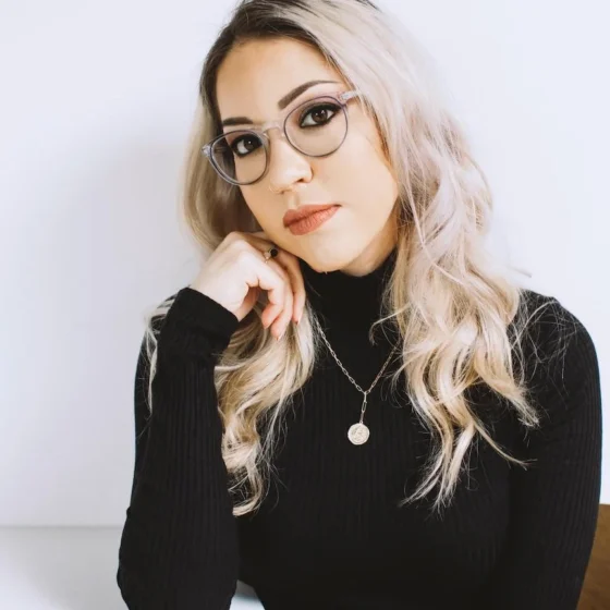 A woman with light blonde, long hair and classes in a black turtleneck and glasses