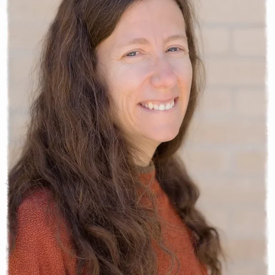 A brunette woman with an orange sweater smiling at the camera