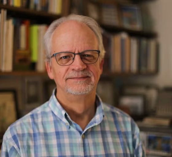A man with white hair, glasses and a blue and white plaid t-shirt