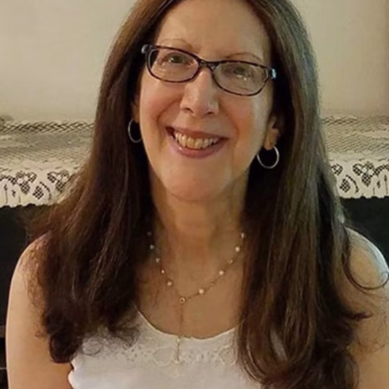 A smiling woman with rectangle glasses and shoulder length brown hair