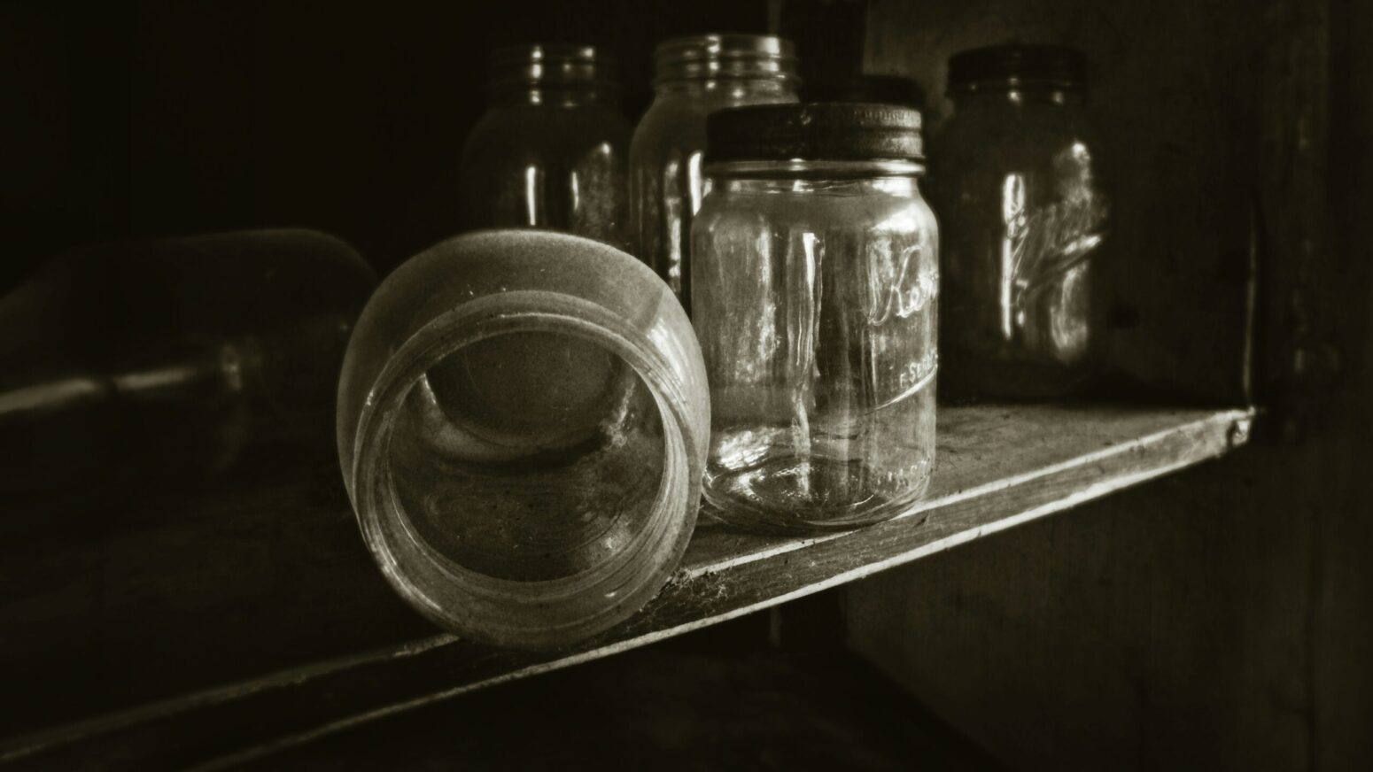 Empty mason jars with a light coat of dust. The jars are on a shelf, with one jar open and tipped over.