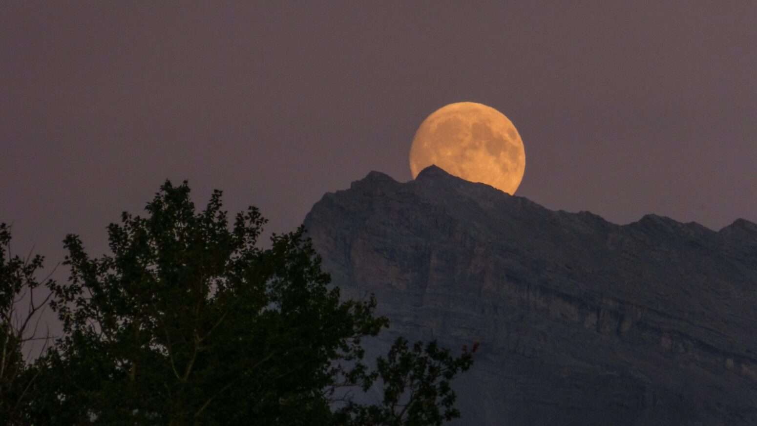 An orange moon rising over a dark mountain range.