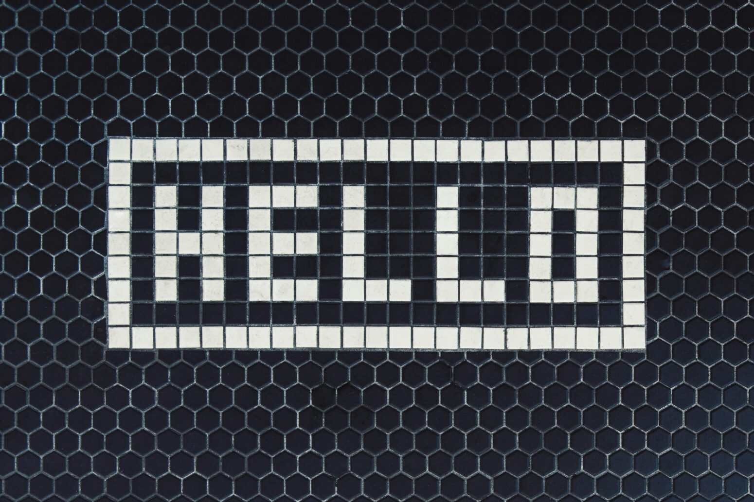 An old-fashioned tile mosaic, spelling out "hello" in all-caps white tile on a black background.