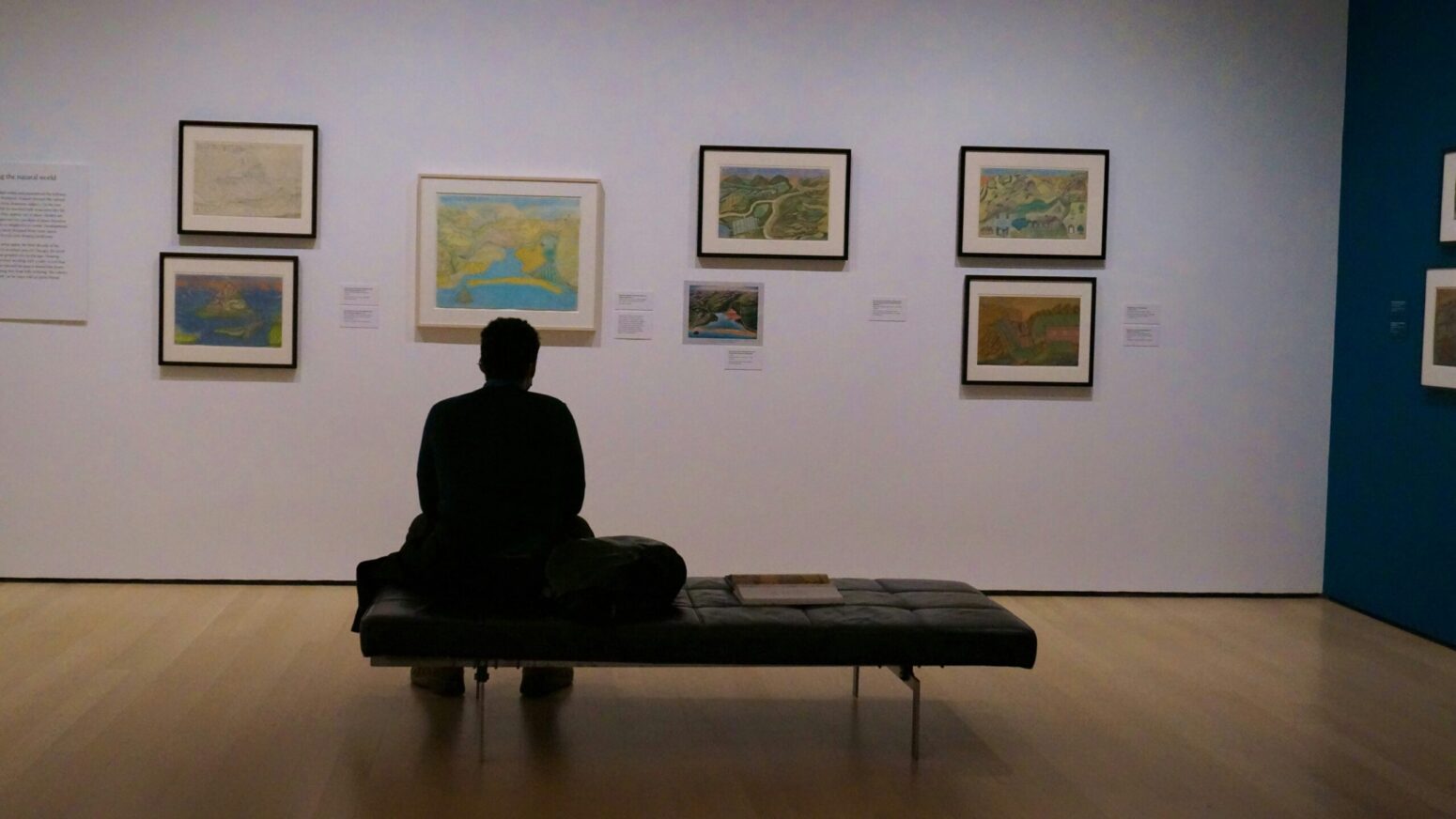 A silhouetted figure sits on a bench in front of a gallery wall.