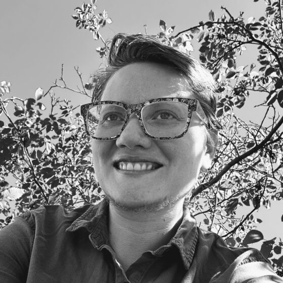 A black and white image of a person with short cropped hair who is smiling and wearing glasses and a collared shirt.