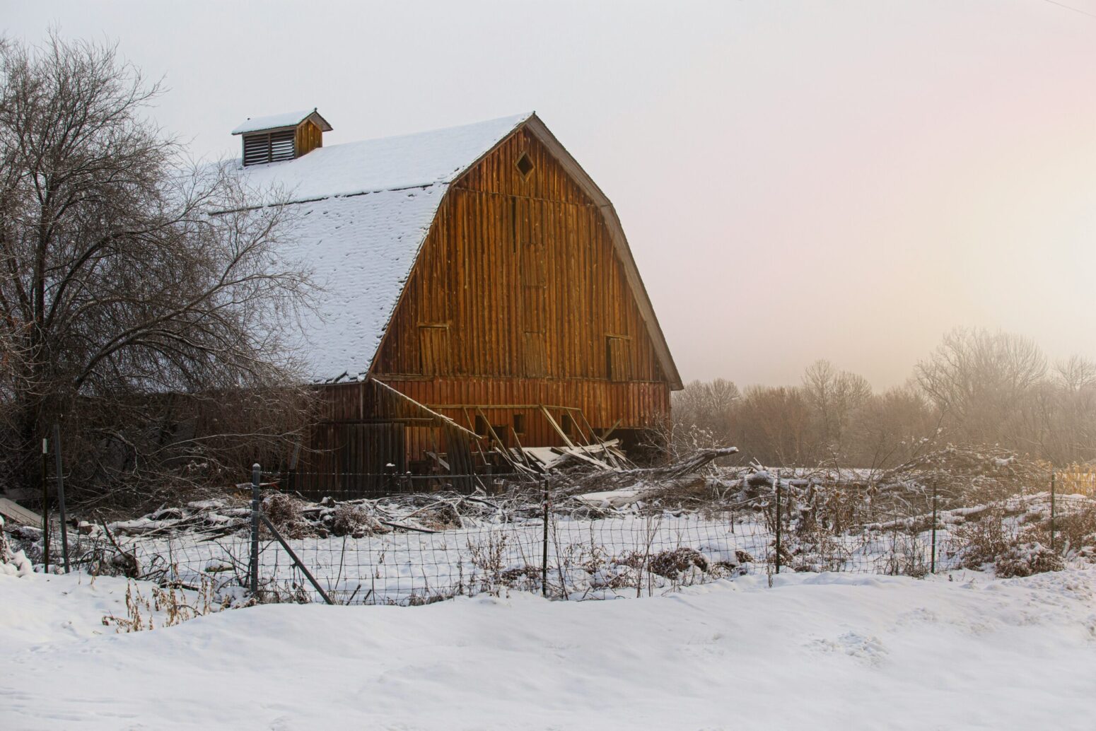 A wood barn lit by a warm glow of daylight is covered with a light layer of snow.