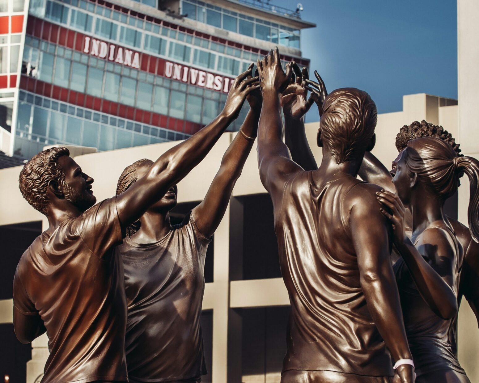 Bronze statues of students in athletic attire high-fiving on the campus of Indiana University.